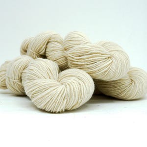 Peut inclure: Plusieurs pelotes de laine blanc cassé, bien enroulées et regroupées. La laine semble douce et texturée, adaptée aux projets de tricot ou de crochet. La couleur neutre suggère une grande polyvalence.