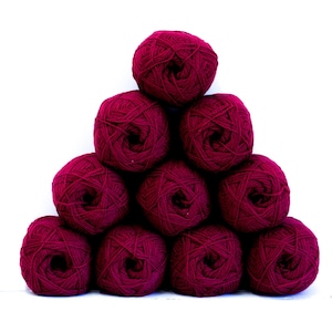 May include: A pyramid arrangement of ten balls of deep burgundy yarn. Each ball is wound into a round, textured sphere, showcasing the rich, dark red color and the twisted fiber construction of the yarn, stacked neatly against a plain white background.