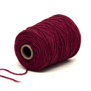 Op de afbeelding: Een grote spoel bordeauxrood garen, ideaal voor brei- of haakprojecten. Het garen is strak gewikkeld rond een kartonnen kern, met een draad die uitsteekt. Het garen heeft een zacht, getextureerd uiterlijk.
