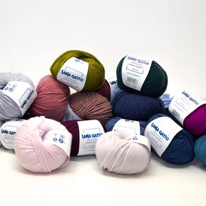 May include: A collection of yarn balls in various colors, including pink, blue, green, white, and purple. The yarn balls are labeled with the text "LANA GATTO" and "HAND SOFT".