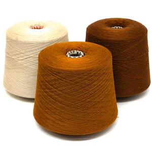 May include: Three cones of yarn in shades of brown and cream against a white backdrop. The yarn is tightly wound around a central core. The colours range from a light cream to a deep brown, suitable for knitting or crochet projects.