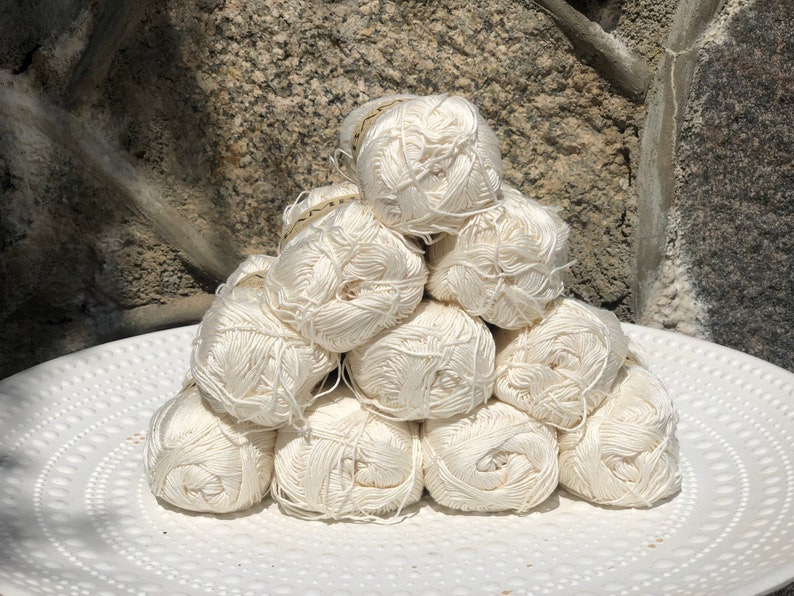 May include: A pile of white yarn balls stacked in a pyramid shape on a white plate with a textured surface.