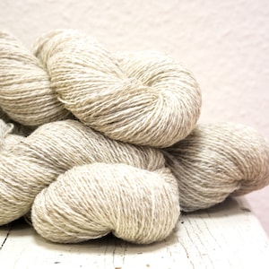 Könnte beinhalten: Ein Stapel beigefarbener Garnknäuel aus Naturfasern, perfekt zum Stricken oder Häkeln.