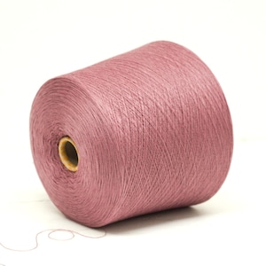 May include: A large spool of dusty rose-colored yarn. The yarn is tightly wound around a cardboard core, with a strand extending from the spool. Ideal for knitting, crocheting, or other fiber arts projects.