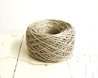 May include: A large, tightly wound ball of natural-colored twine. The twine is a light brown color and appears to be made of a natural fiber. The ball of twine sits on a white, weathered wooden surface.