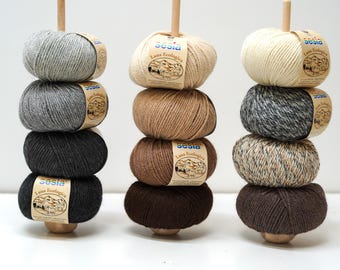 Könnte beinhalten: Drei Stapel Garn in verschiedenen Grau-, Beige- und Brauntönen. Jeder Stapel hat vier Knäuel, mit einem Holzstab in der Mitte. Das Garn hat Etiketten mit der Aufschrift "sesia Lana Ecologica".