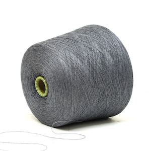 May include: A large spool of grey yarn, suitable for knitting or crochet projects. The yarn is tightly wound, with a visible thread extending from the spool. The core of the spool is a light green colour.