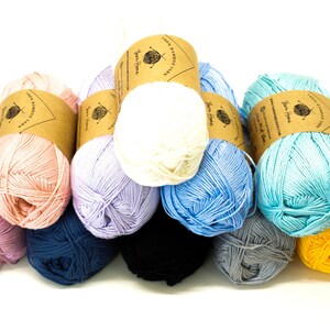 May include: A collection of eight skeins of 100% bamboo yarn in various colors, including pink, lavender, blue, white, and yellow. Each skein has a brown paper label with the text "Yarn Home" and "100% Bamboo Cotton Yarn".