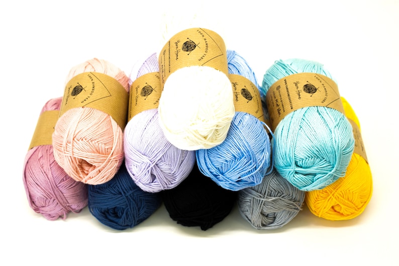May include: A collection of eight skeins of 100% bamboo yarn in various colors, including pink, lavender, blue, white, and yellow. Each skein has a brown paper label with the text "Yarn Home" and "100% Bamboo Cotton Yarn".