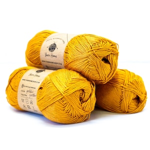 以下が含まれることがあります： 「Yarn Home」と「Golden Yellow」の文字が書かれた茶色のラベルが付いた、金色がかった黄色の糸のボールが3つ。糸の扱い方についての説明も書かれています。