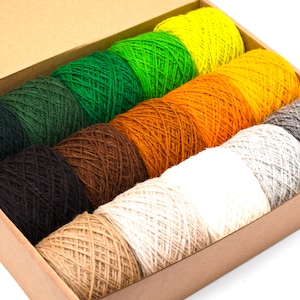 May include: A box containing ten balls of yarn in a variety of colours, including green, brown, orange, yellow, white and grey. The yarn is arranged in a rainbow pattern.