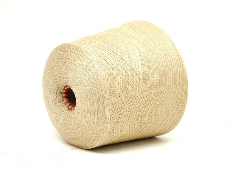 May include: A large spool of beige yarn, tightly wound with visible thread lines. The center hole reveals a red and white striped core. Ideal for knitting, crocheting, or other fiber crafts.