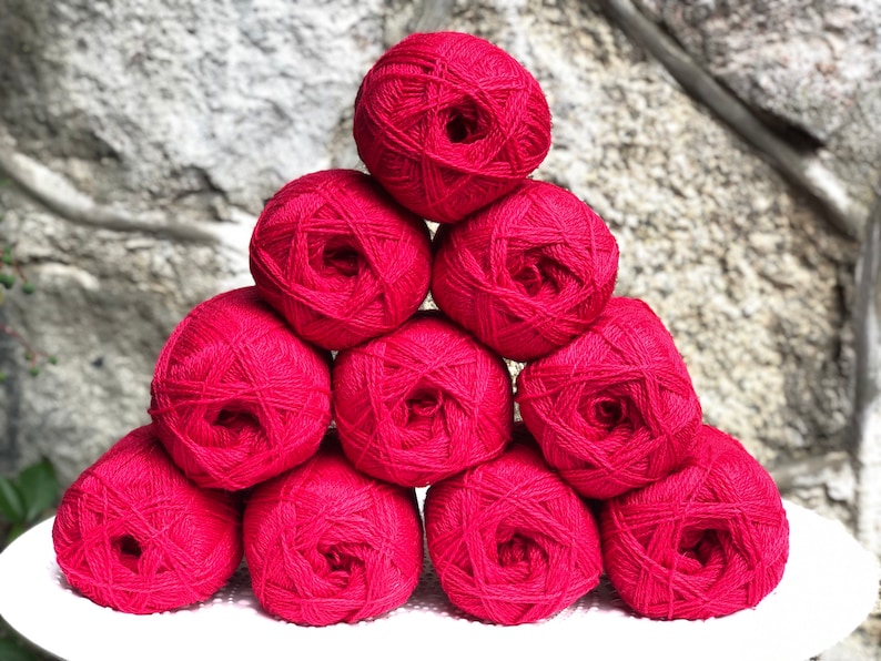 May include: A pile of nine red yarn balls stacked in a pyramid shape.