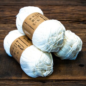 May include: Three balls of white cotton yarn with brown paper labels. The labels have instructions for washing and drying the yarn. The labels also say "Made in Lithuania" and "Yarn Home".