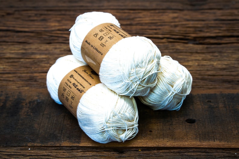 May include: Three balls of white cotton yarn with brown paper labels. The labels have instructions for washing and drying the yarn. The labels also say "Made in Lithuania" and "Yarn Home".