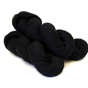 Könnte beinhalten: Nahaufnahme von mehreren Strängen schwarzer Wolle, ideal für Strick- oder Häkelprojekte. Das Garn hat eine einfarbige, tiefschwarze Farbe und die Textur erscheint weich und leicht flauschig. Die Stränge sind auf weißem Hintergrund angeordnet.