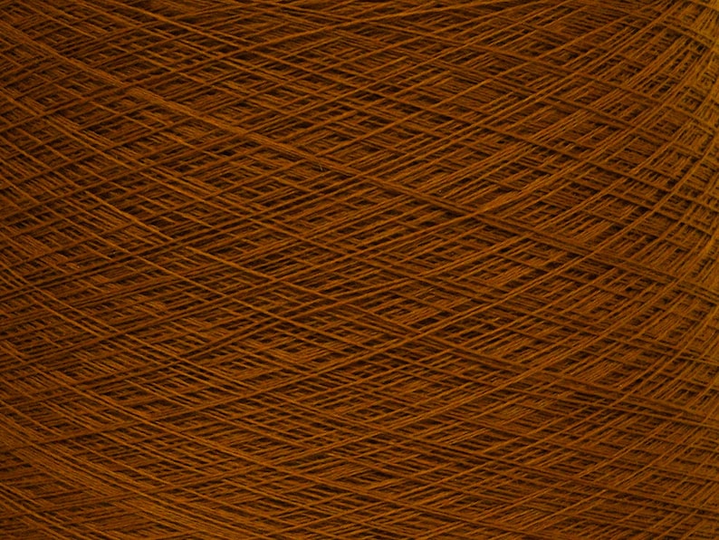May include: Close-up of a tightly wound ball of brown yarn. The yarn is a warm, earthy tone, with visible strands creating a textured surface. The image highlights the intricate pattern of the yarn, suggesting its use in knitting or other crafts.