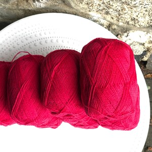 May include: Four balls of bright red yarn are stacked on a white plate. The yarn is soft and fluffy, and it would be perfect for knitting or crocheting.