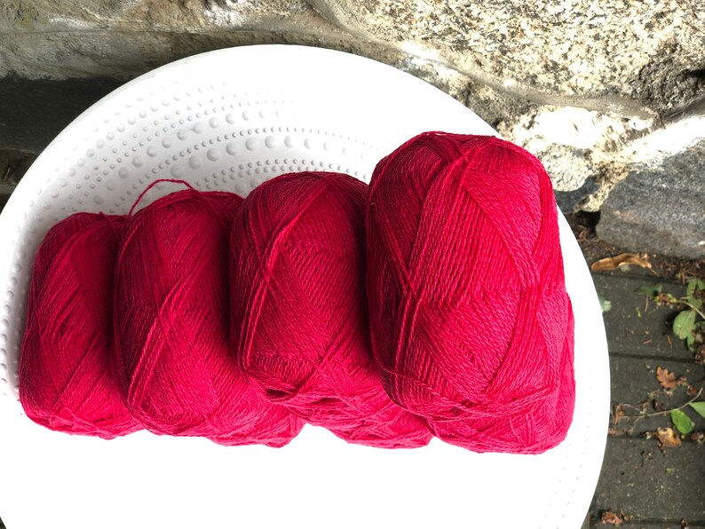 May include: Four balls of bright red yarn are stacked on a white plate. The yarn is soft and fluffy, and it would be perfect for knitting or crocheting.