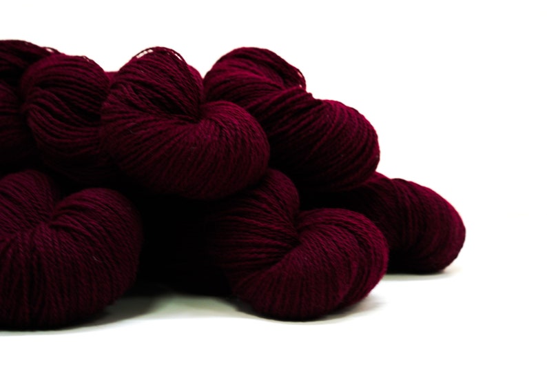 May include: A pile of deep burgundy yarn skeins. The yarn is soft and fluffy, perfect for knitting or crocheting.