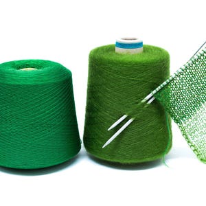 May include: Two spools of green yarn, one with a fluffy texture and one with a smooth texture, with knitting needles and a green knitted fabric sample.