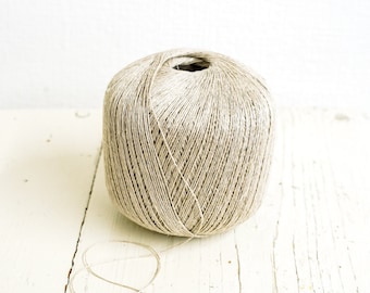 May include: A ball of natural beige yarn, wound into a neat coil, sits on a white wooden surface.