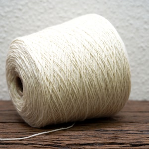 Puede incluir: Un carrete de hilo blanco natural, enrollado firmemente y listo para tejer o hacer ganchillo. El hilo es suave y liso, con un brillo sutil.
