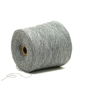 Peut inclure: Une grosse bobine de fil gris, idéale pour les projets de tricot ou de crochet. Le fil est enroulé serré autour d'un noyau en carton, avec un brin qui s'étend de la bobine. Le fil semble doux et a un léger éclat.