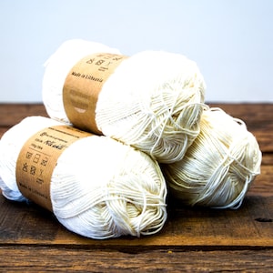 May include: Three balls of white cotton yarn with brown paper labels that say "Made in Lithuania" and include washing instructions.