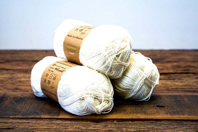 May include: Three balls of white cotton yarn with brown paper labels that say "Made in Lithuania" and include washing instructions.