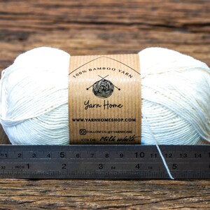 May include: A ball of 100% bamboo yarn in milk white color, with a brown label that says "Yarn Home" and "www.yarnhomeshop.com". The yarn is measured with a ruler in inches.