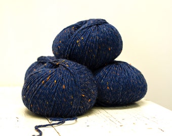 Puede incluir: Tres ovillos de hilo azul marino con motas de color naranja. El hilo está apilado sobre una superficie blanca.