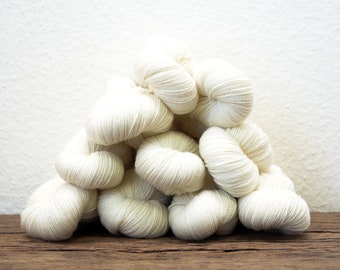 May include: A pile of white yarn balls, likely for knitting or crocheting, arranged on a wooden surface.