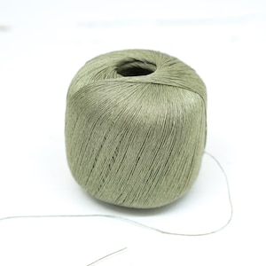 Puede incluir: Una bola de hilo verde con un hilo largo que se extiende desde ella.