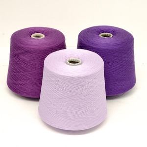 Puede incluir: Tres conos de hilo en tonos morados y lavanda. El hilo está enrollado firmemente alrededor de núcleos de cartón, creando una forma cónica. Los colores varían de un violeta intenso a un lavanda suave y pálido.