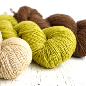 Könnte beinhalten: Drei Knäuel Garn in beige, grün und braun. Das Garn ist in Herzform angeordnet.