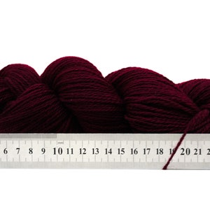May include: A skein of deep burgundy yarn, measured against a ruler with markings from 2 to 25.