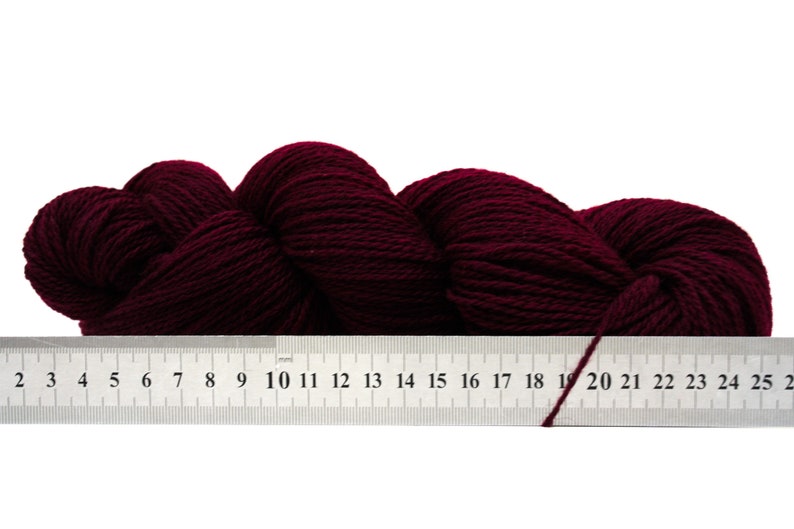 May include: A skein of deep burgundy yarn, measured against a ruler with markings from 2 to 25.