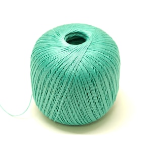 Puede incluir: Una bola de hilo de color verde azulado con un hilo largo que se extiende desde ella.
