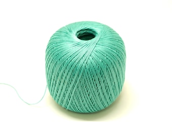 Puede incluir: Una bola de hilo de color verde azulado con un hilo largo que se extiende desde ella.
