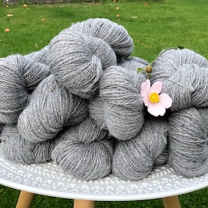 May include: A pile of gray yarn skeins on a white plate with a pink flower on top.