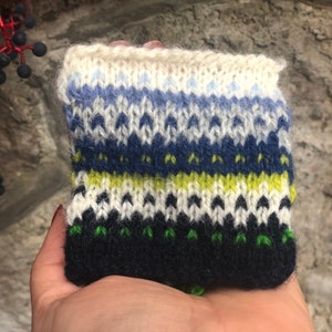 May include: A knitted fabric swatch with a colorful pattern in shades of blue, green, yellow, and white. The fabric is made with a variety of stitches, creating a textured look.