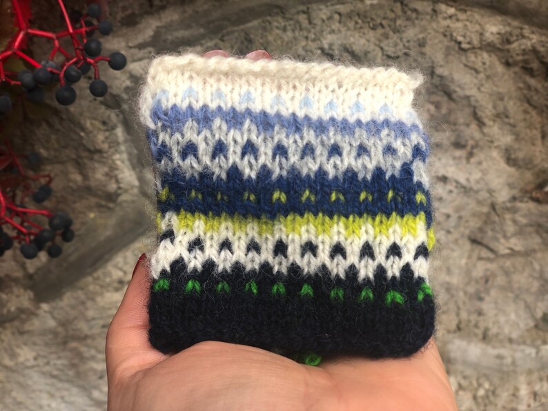 May include: A knitted fabric swatch with a colorful pattern in shades of blue, green, yellow, and white. The fabric is made with a variety of stitches, creating a textured look.