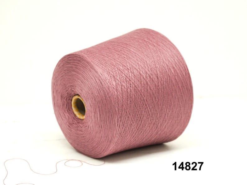 May include: A large spool of dusty rose-colored yarn. The yarn is tightly wound around a cardboard core. The number "14827" is printed in black on the lower right corner. The yarn is on a white background.