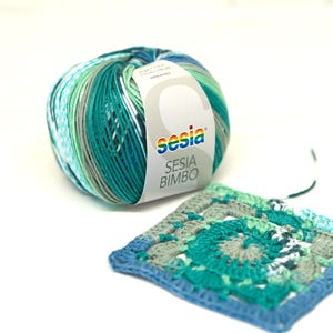 May include: A ball of Sesia Bimbo yarn in shades of teal, green, and gray, with a matching crocheted square. The yarn label is white with the Sesia logo and product information. The crocheted square features a spiral design.