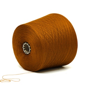 May include: A large spool of brown yarn, ideal for knitting or crocheting projects. The yarn is tightly wound around a white core with a patterned edge. A strand of yarn extends from the spool, suggesting its use. The background is plain white.