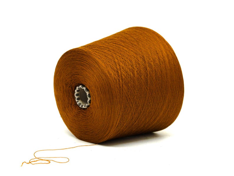 May include: A large spool of brown yarn, ideal for knitting or crocheting projects. The yarn is tightly wound around a white core with a patterned edge. A strand of yarn extends from the spool, suggesting its use. The background is plain white.