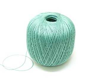 Puede incluir: Una bola de hilo de color verde claro con un solo hilo que se extiende de la bola.