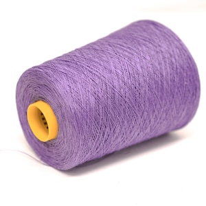 May include: A large spool of lavender-coloured yarn wound tightly around a cylindrical core. The spool features a bright yellow plastic centre insert with a small hole, and a single thin strand of the purple thread extends from the bottom left.