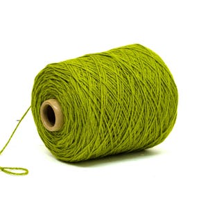 May include: A large spool of vibrant green yarn, suitable for knitting or crochet. The yarn is tightly wound around a cardboard core, with a strand extending outwards. The background is plain white.